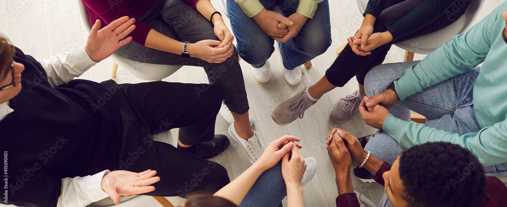 Top view of diverse people sitting in a close circle and talking to a therapist. Cropped image of unidentified people receive help and support during a group therapy session. Concept of group therapy.